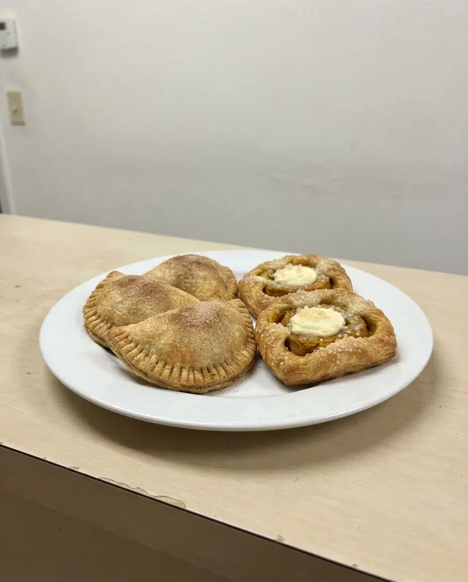 A plain phone photo of apple hand pies and pumpkin danishes on a white plate on a bare counter